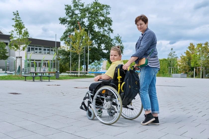 Disabled boy in wheelchair with support worker both smiling at camera